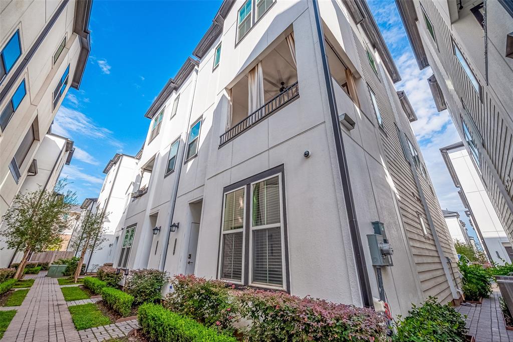 This is a modern townhouse complex with a well-manicured communal garden pathway. The buildings feature a contemporary design with multiple levels, large windows, and private balconies. The exterior is finished in neutral tones, complementing the urban landscape.