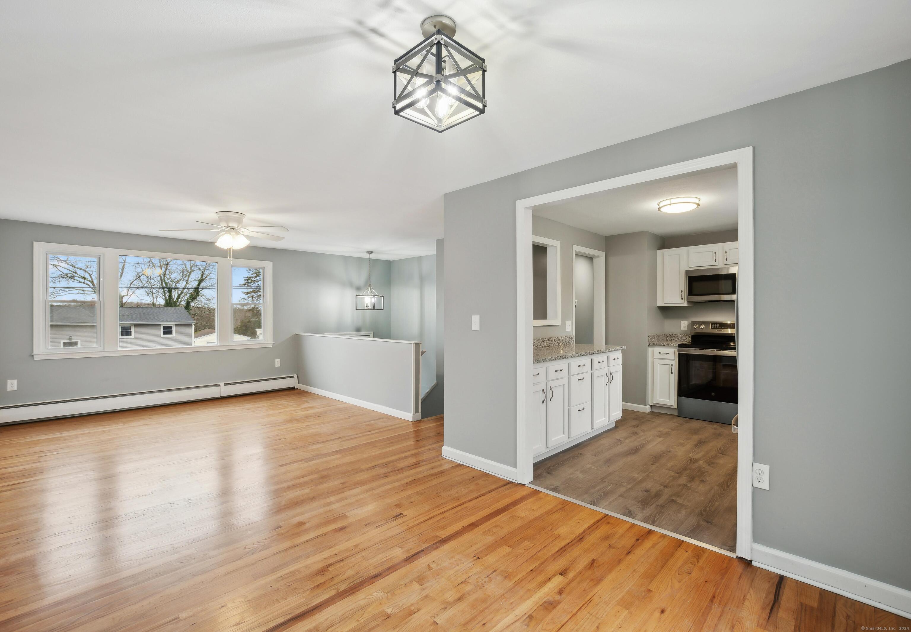 a view of an empty room with wooden floor and a kitchen