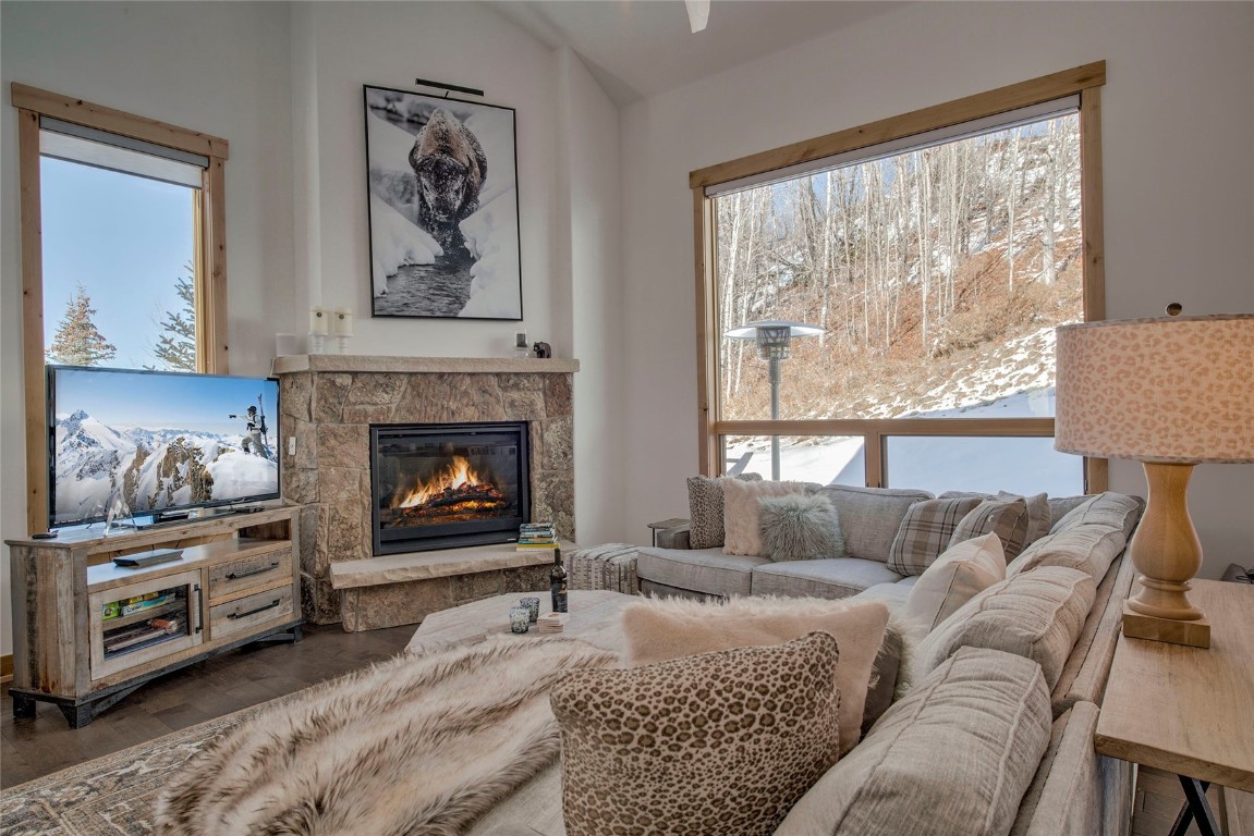 Living room featuring dark hardwood / wood-style floors, a stone fireplace, and lofted ceiling