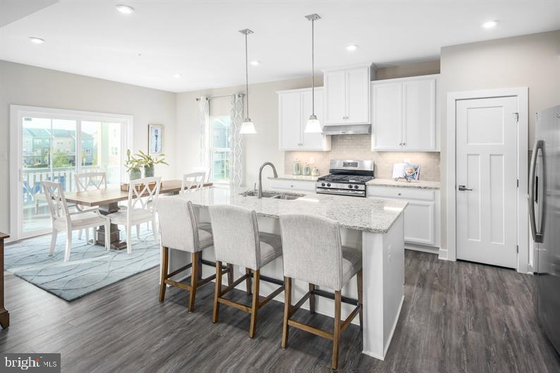 a kitchen with stainless steel appliances granite countertop a stove a refrigerator a kitchen island a dining table and chairs with wooden floor