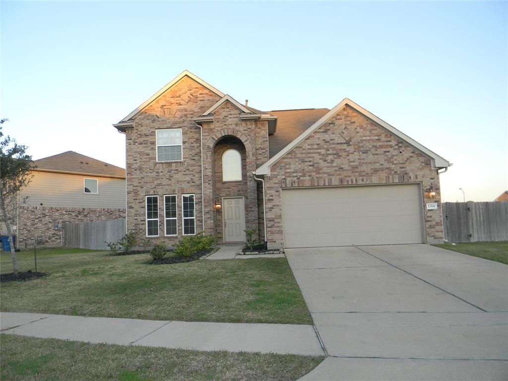 This is a two-story brick home with a two-car garage, a neatly maintained front yard, and a welcoming entrance with an arched doorway. The property is enclosed with a wooden fence, providing privacy.