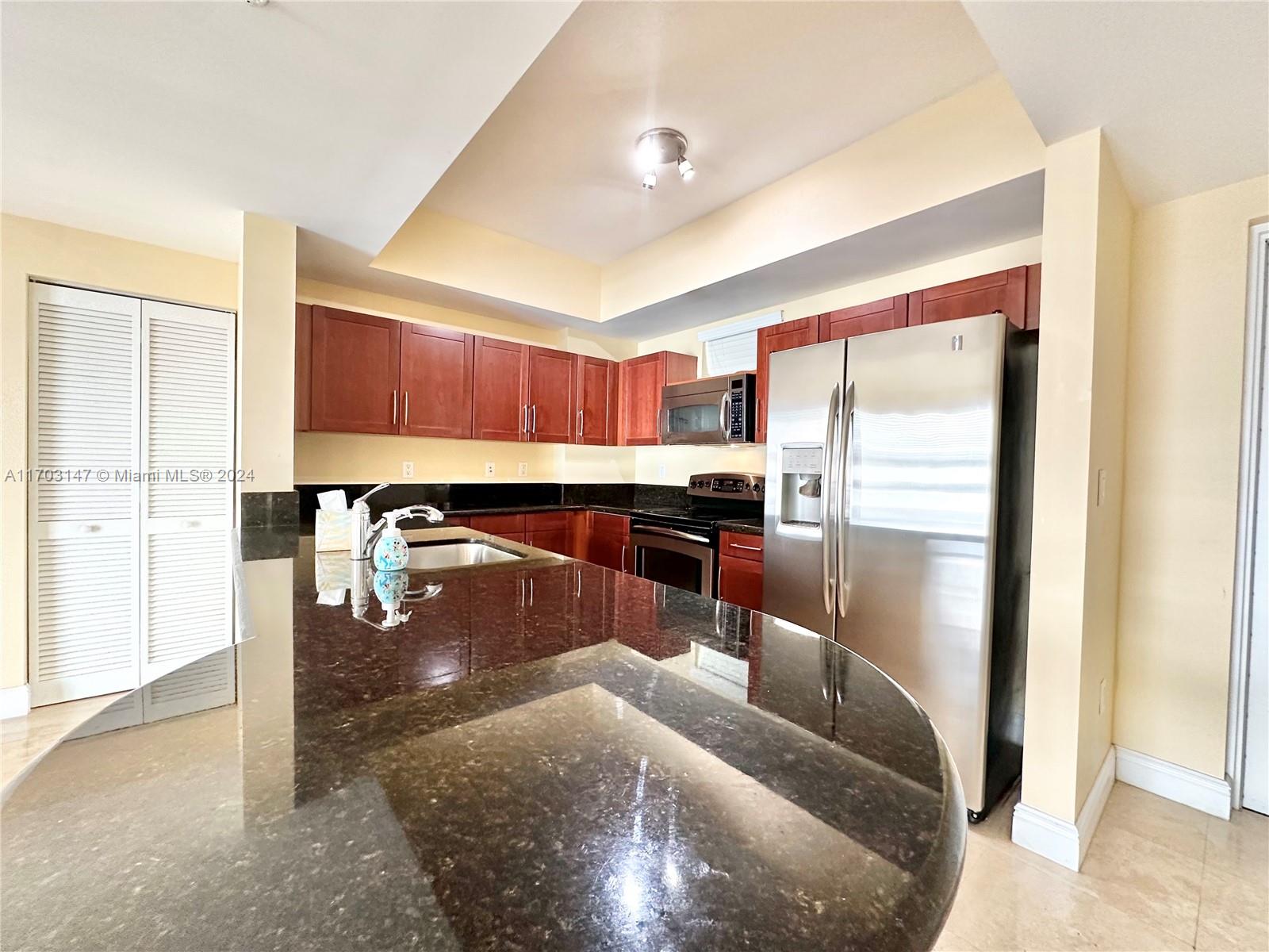 a kitchen with stainless steel appliances granite countertop a refrigerator and a view of living room