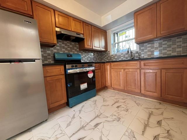 Kitchen featuring tasteful backsplash, stainless steel fridge, sink, and black range