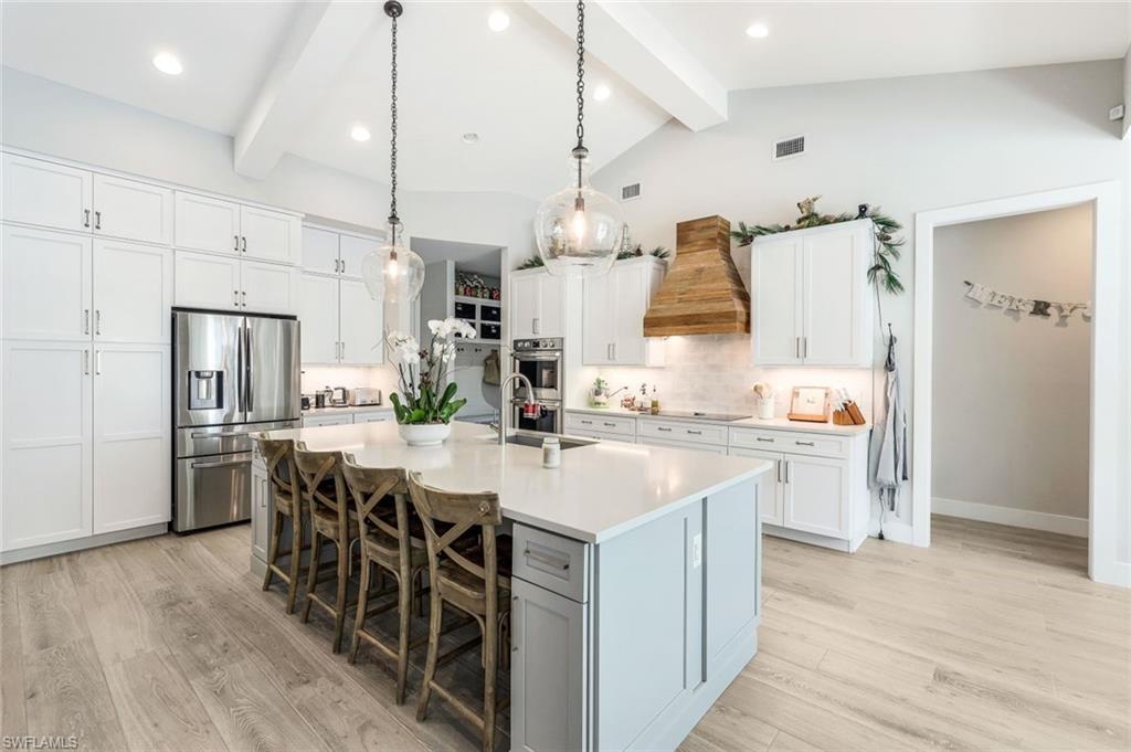 Kitchen with white cabinets, a center island with sink, custom range hood, and stainless steel appliances