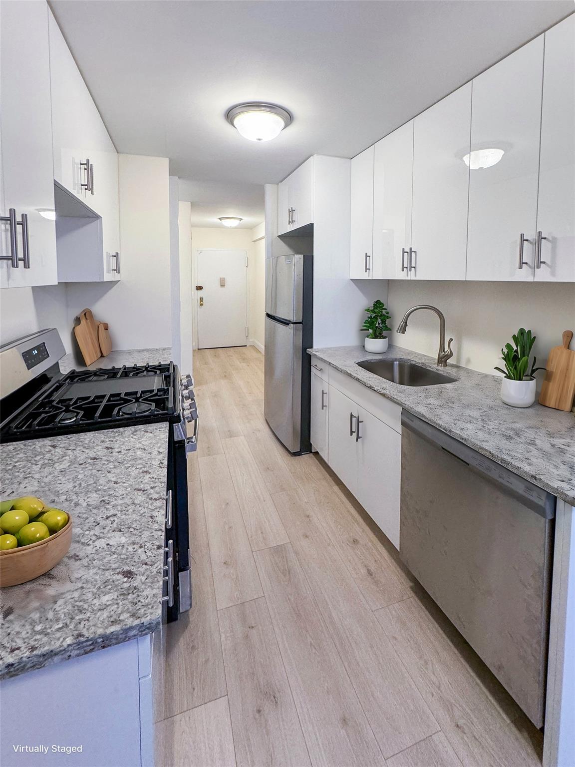 Kitchen with white cabinetry, sink, light vinyl plank floors, and appliances with stainless steel finishes- Virtually staged