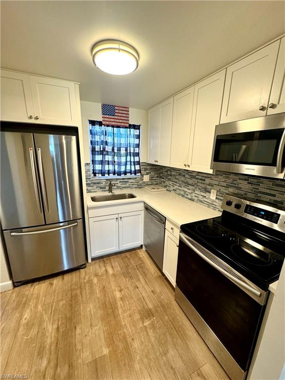 Kitchen with white cabinets, sink, light wood-type flooring, tasteful backsplash, and stainless steel appliances