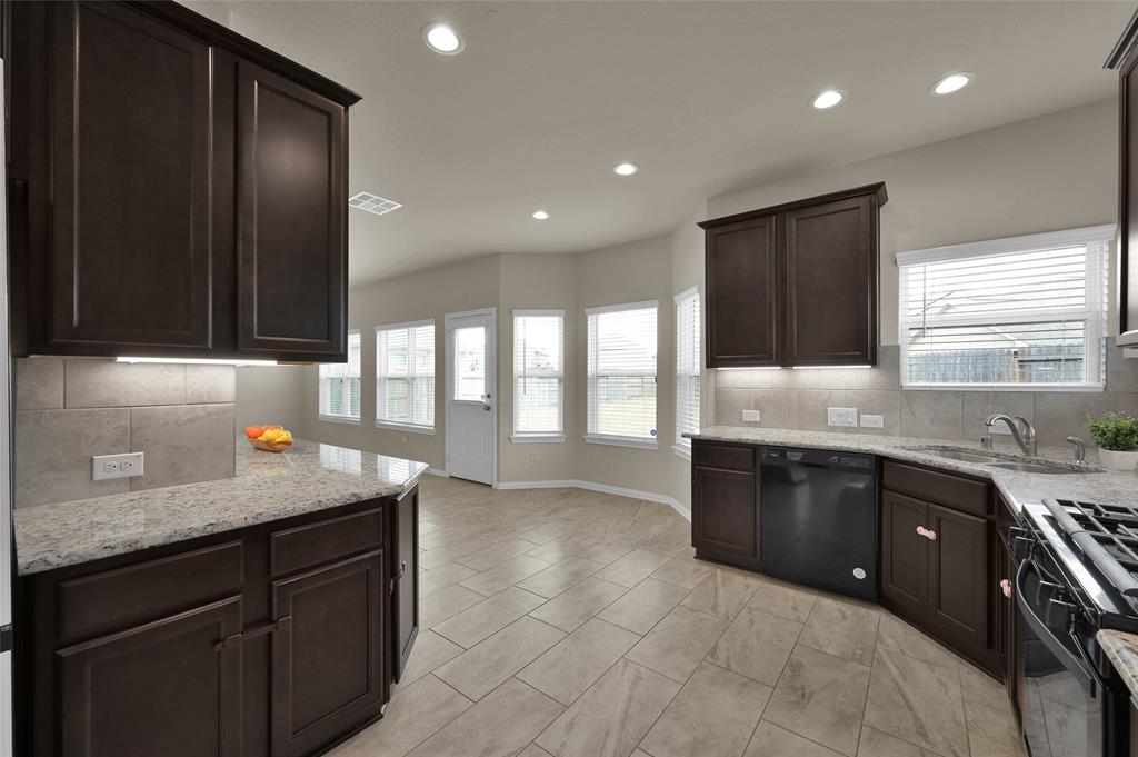 This is a spacious modern kitchen featuring dark wood cabinets, granite countertops, plenty of counterspace, and tiled flooring. Natural light floods the room through multiple windows. 