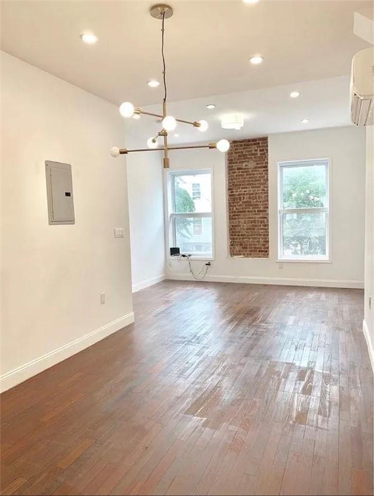 Unfurnished living room featuring plenty of natural light, dark wood-type flooring, a wall mounted AC, and electric panel