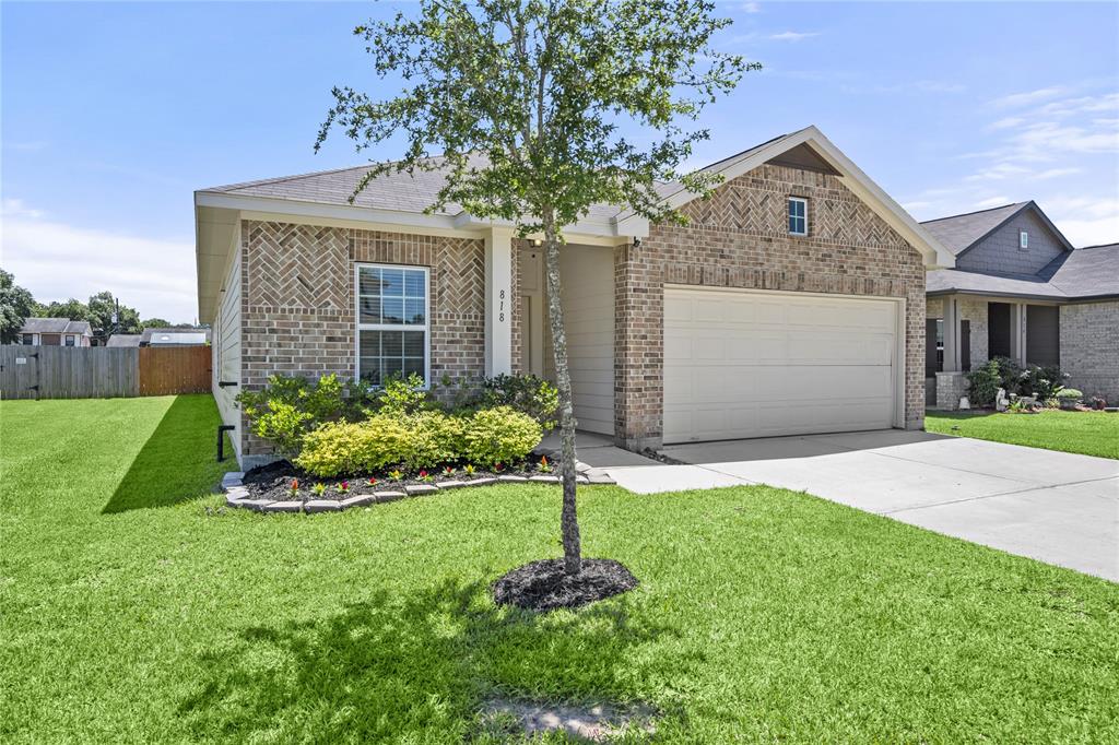 This is a single-story brick home featuring a well-manicured lawn, an attached two-car garage, and a welcoming landscaping bed with shrubs and flowers.