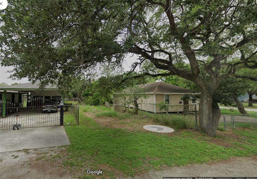 a view of a white house in front of a yard with plants and large trees