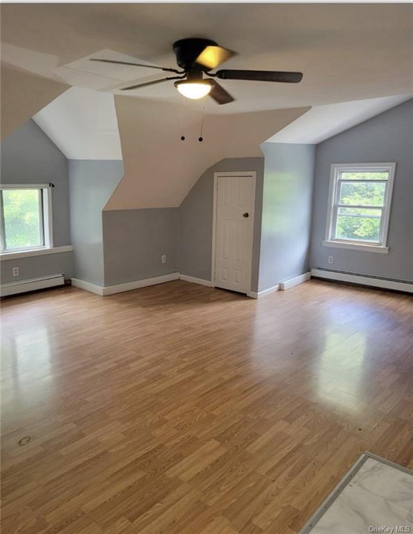 Additional living space featuring ceiling fan, light hardwood / wood-style flooring, baseboard heating, and lofted ceiling