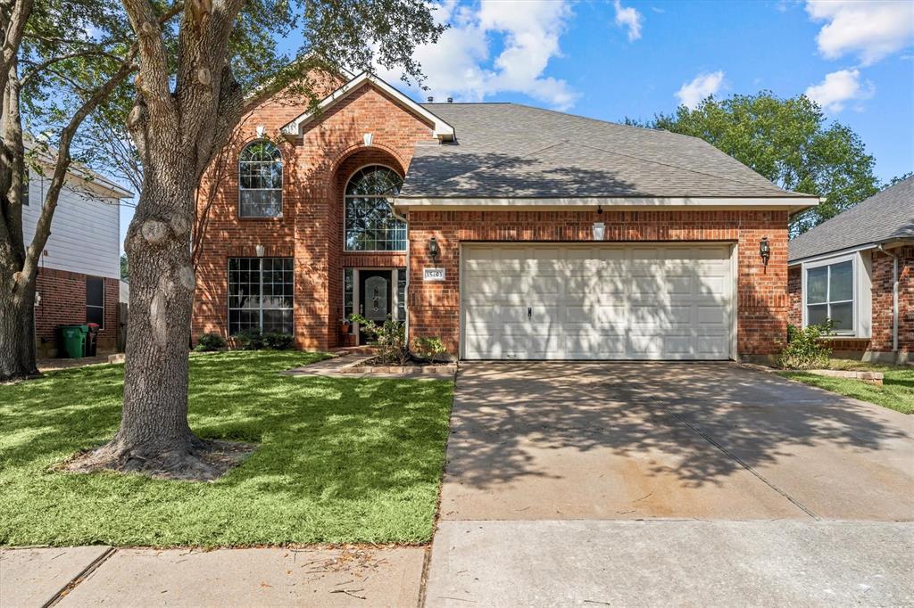 This is a two-story brick home featuring a large arched window, an attached two-car garage, and a well-maintained lawn with mature trees.