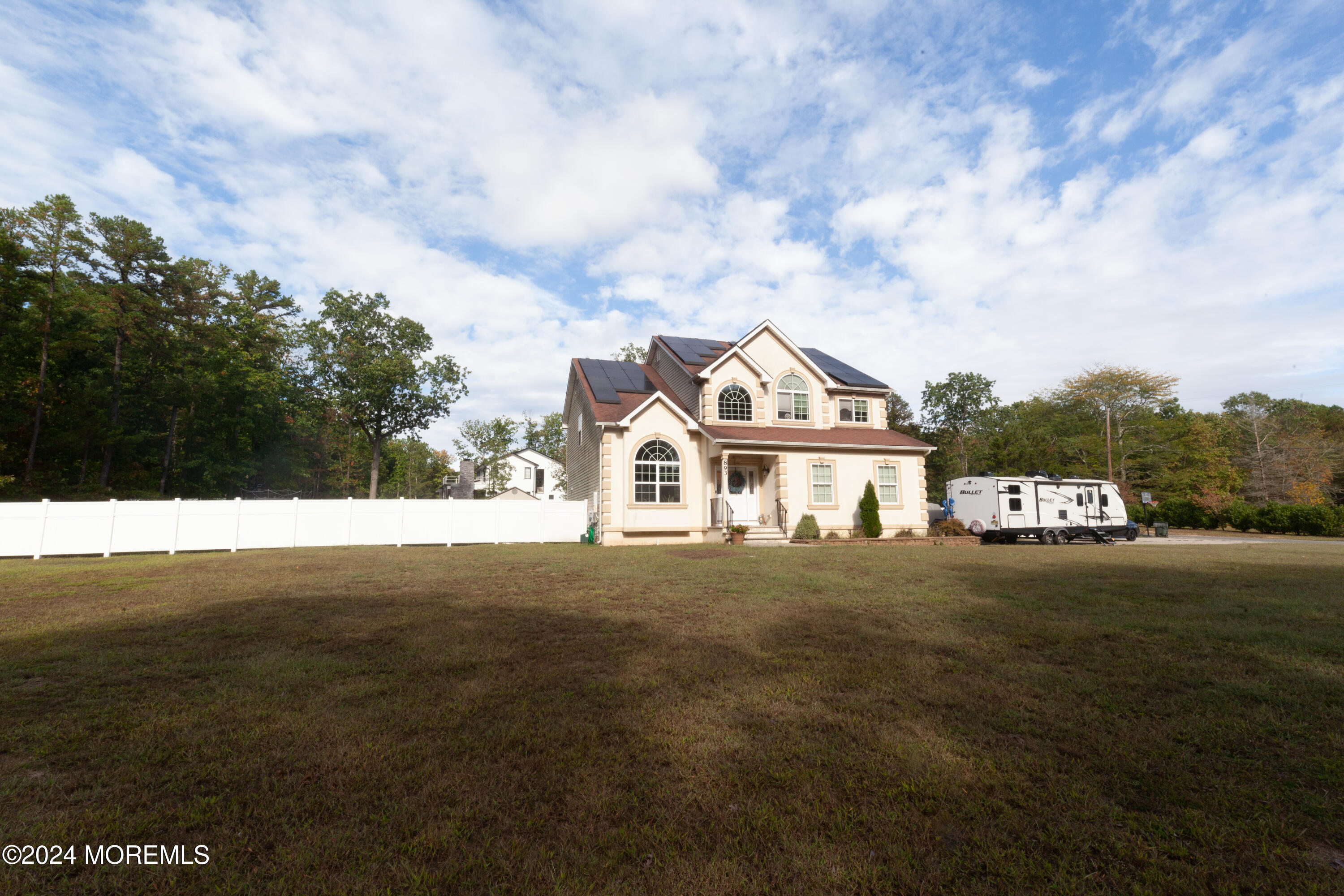 a view of a white house next to a yard with large trees