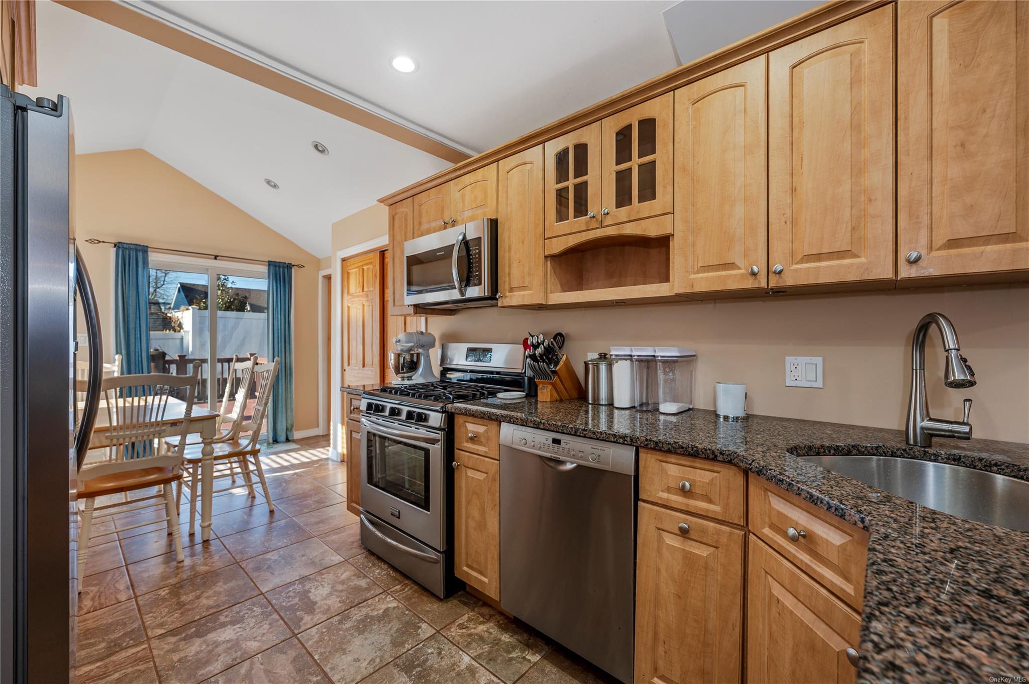 Kitchen featuring appliances with stainless steel finishes, dark stone countertops, lofted ceiling, and sink