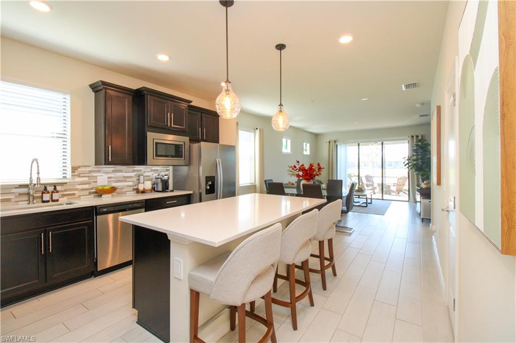 Kitchen featuring sink, appliances with stainless steel finishes, decorative light fixtures, a kitchen island, and a breakfast bar area