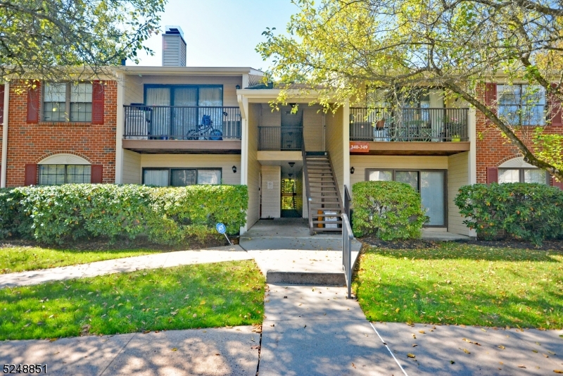 a view of a brick house with a yard plants and large tree