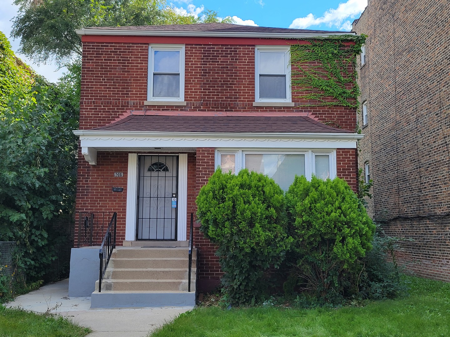 a view of a house with brick walls and a yard with plants and large trees