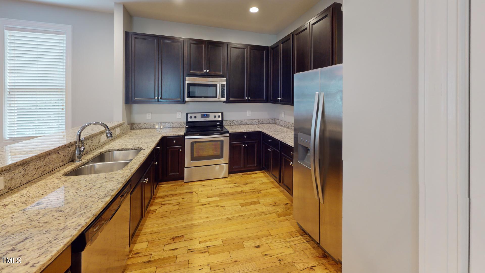 a kitchen with stainless steel appliances granite countertop a sink a stove a refrigerator a washer dryer and cabinets