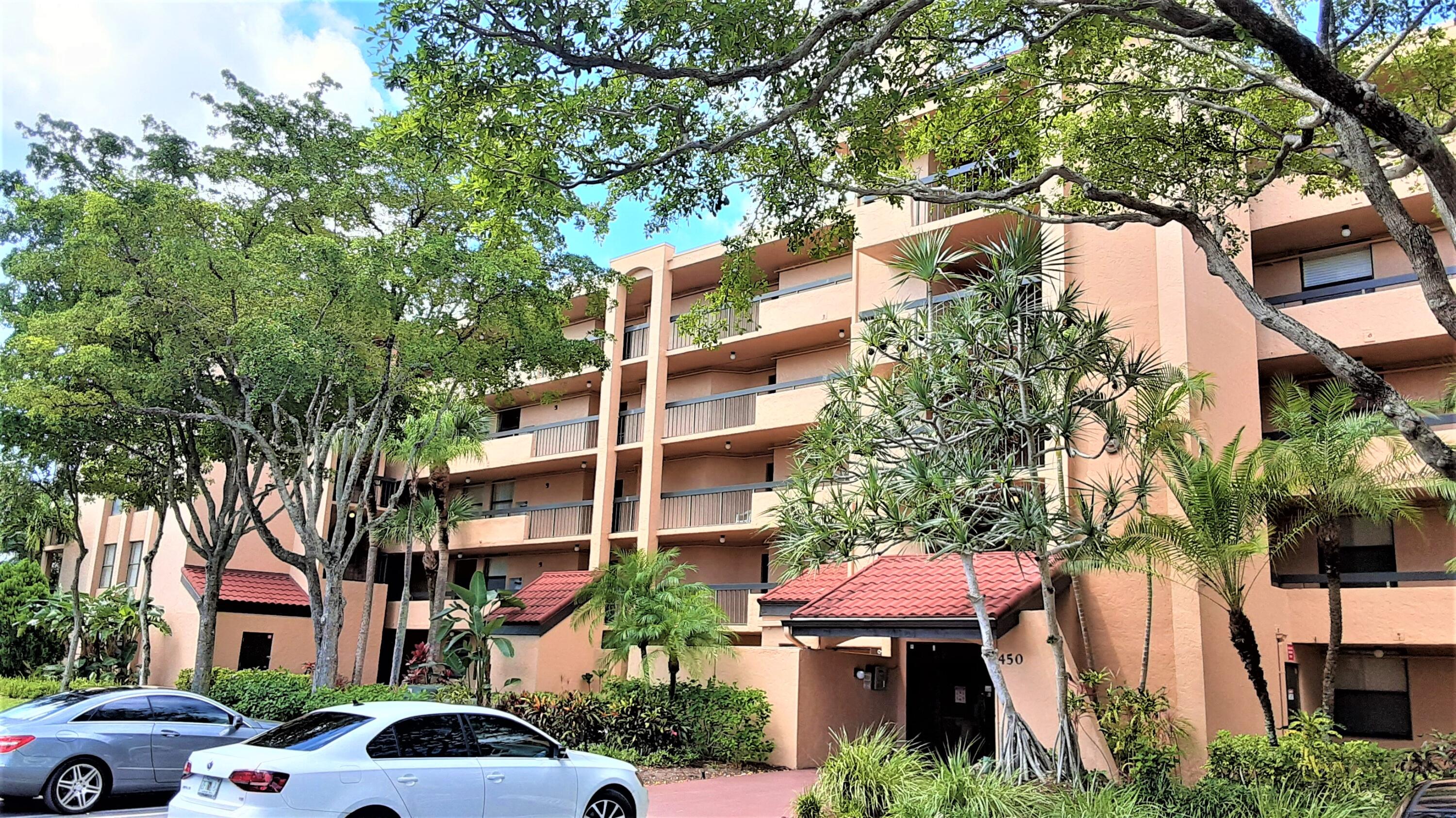 a front view of a building with a garden and trees