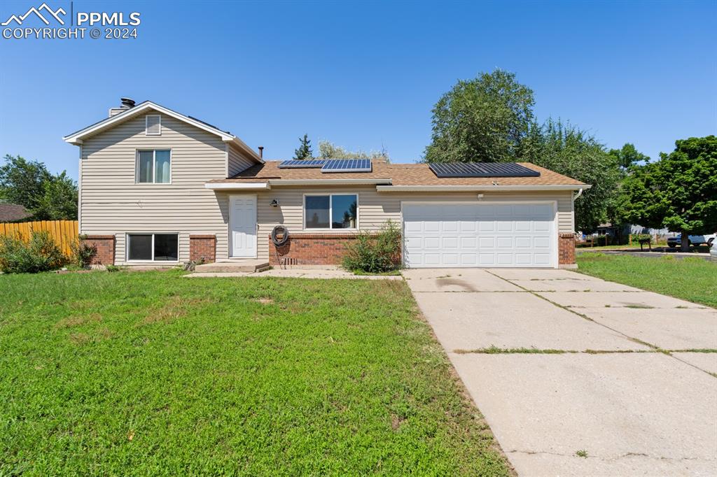 Split level home featuring a garage, a front yard, and solar panels