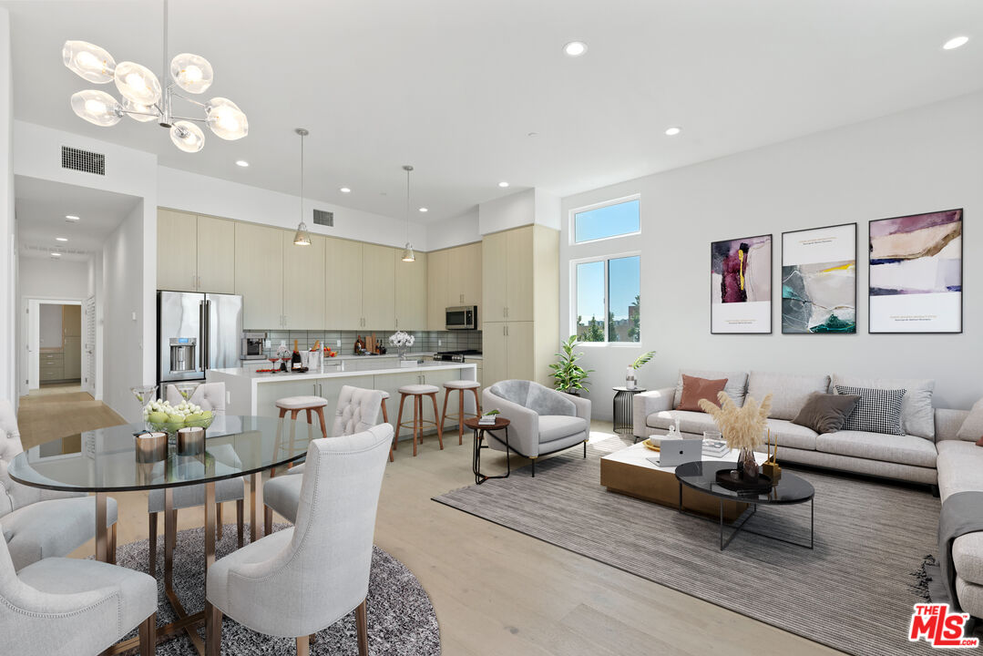 a living room with white couches and kitchen view with wooden floor