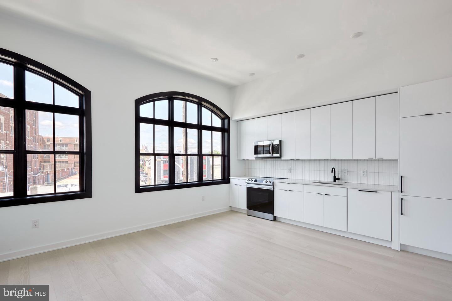 a large white kitchen with stainless steel appliances granite countertop a stove a sink and a large window