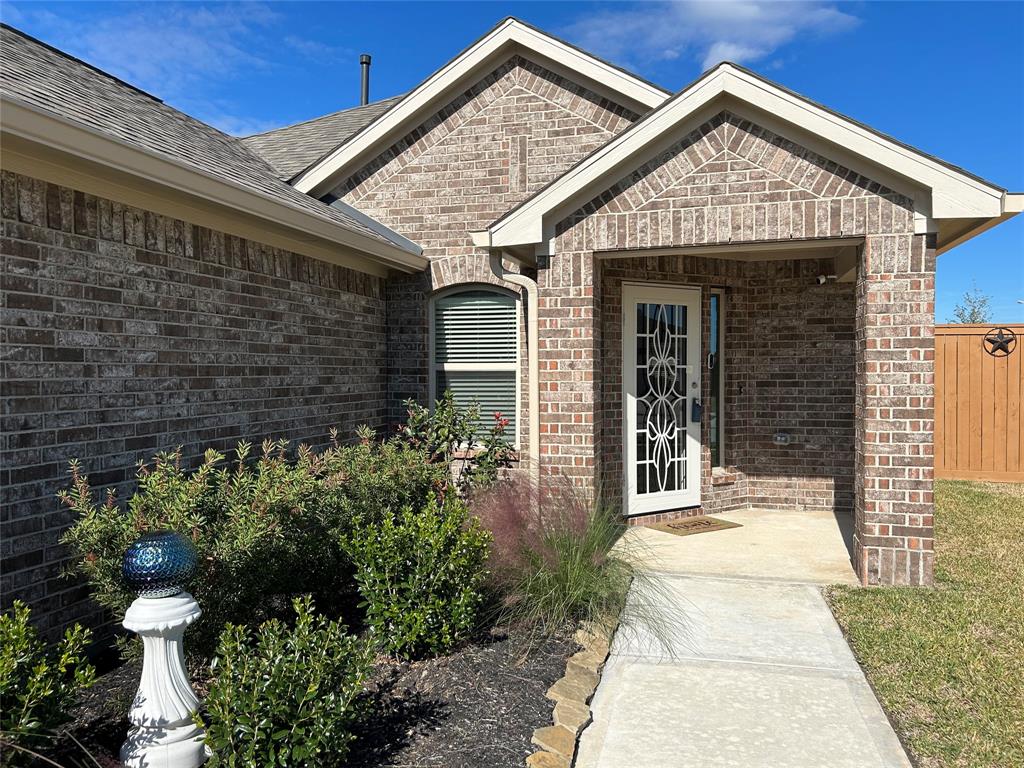 This photo features a charming brick home with a welcoming front entrance. It has a covered porch, decorative glass door, and well-maintained landscaping. The pathway leads to the door, enhancing the inviting feel of the property.