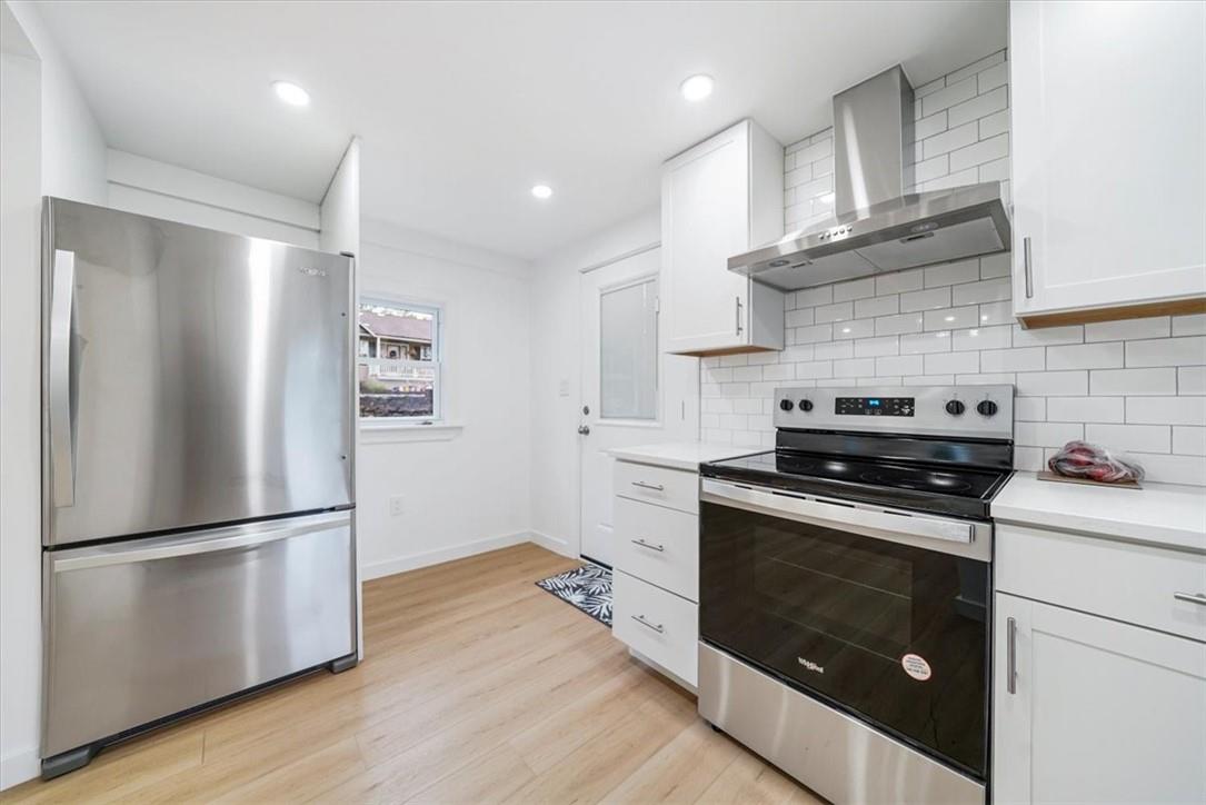 Kitchen featuring wall chimney range hood, backsplash, appliances with stainless steel finishes, and light hardwood floors