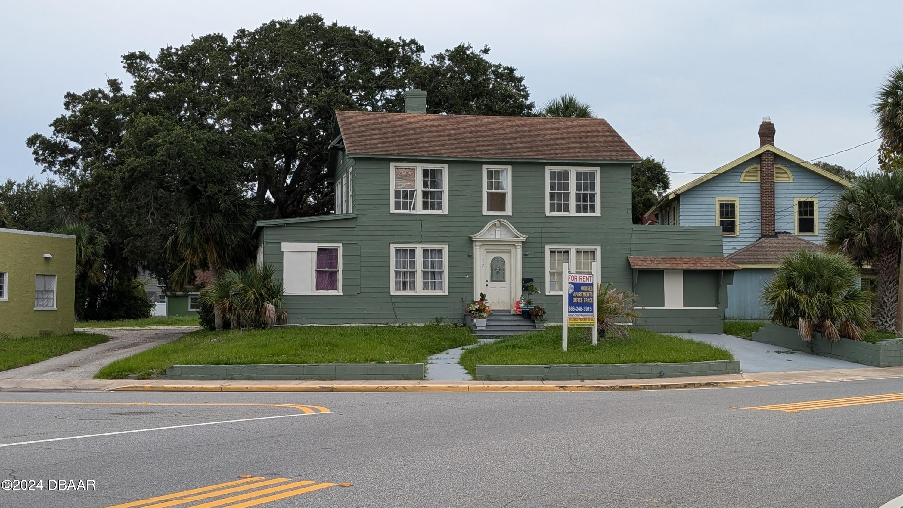 a view of a brick house with a yard plants and a large tree