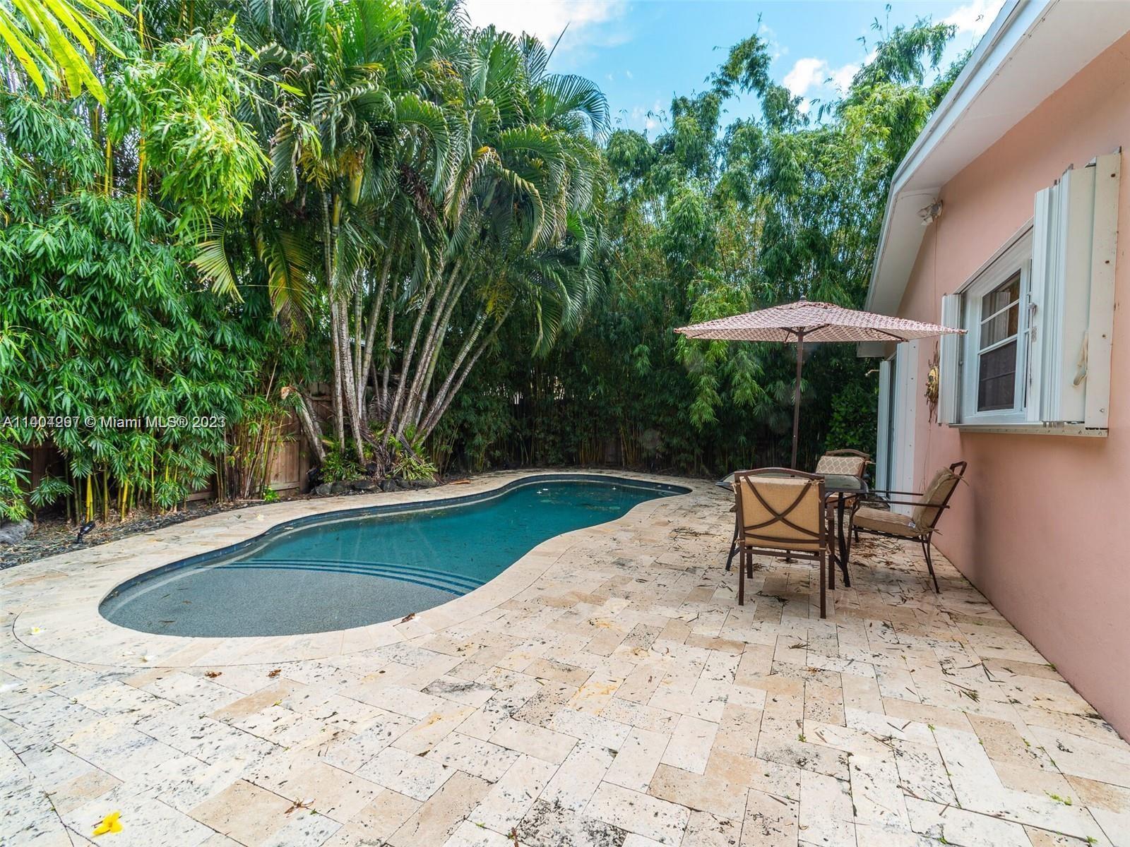 a view of backyard with swimming pool and table and chairs under an umbrella