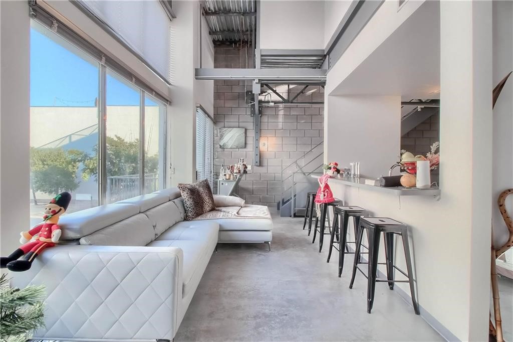 Great living space with wall of windows to the left, gourmet kitchen on the right and stairway to primary bedroom suite and rooftop terrace at the far end of the living room.