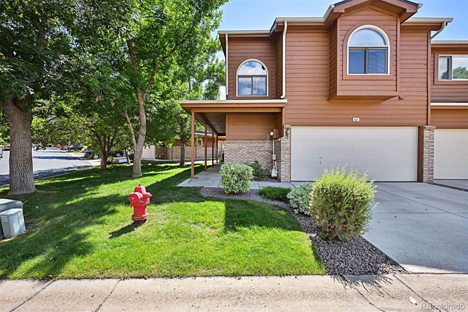 a view of a brick house with a yard plants and a large tree