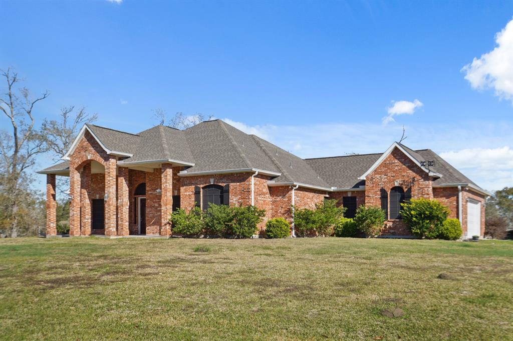 This photo shows a beautiful single-story brick home with a pitched roof. The house features large arches and a welcoming front porch, surrounded by a well-maintained lawn and shrubs.