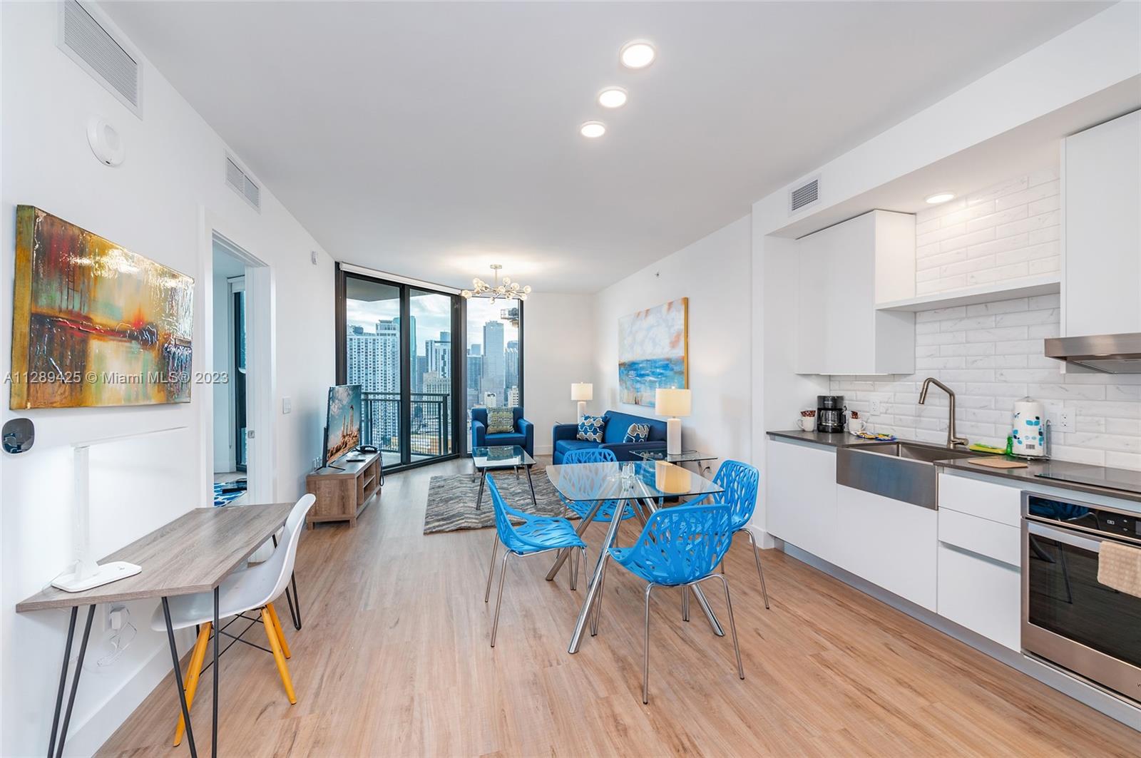 a living room with dining table wooden floor and stainless steel appliances