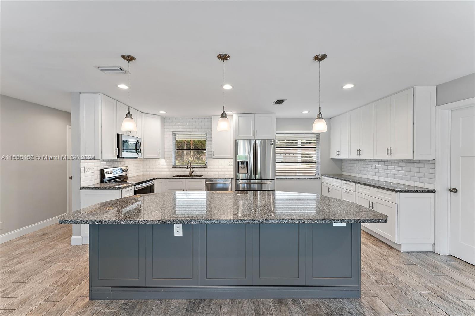 a large kitchen with kitchen island a large counter top stainless steel appliances and cabinets