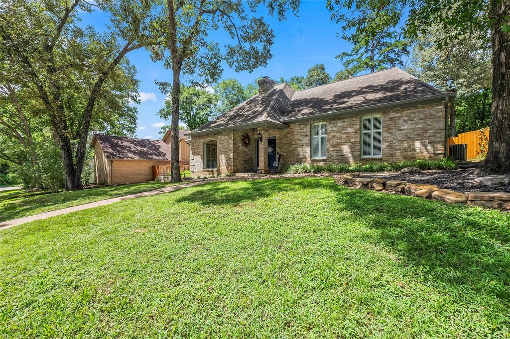 Another view of the front lush green lawn, trees, and walkway leading to the charming brick house with a welcoming entrance.