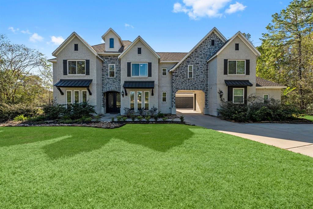 This is a spacious two-story home featuring a stone and stucco exterior, steep gabled roofs, and a garage. The property includes well-manicured lawns and landscaping with mature trees in the background.