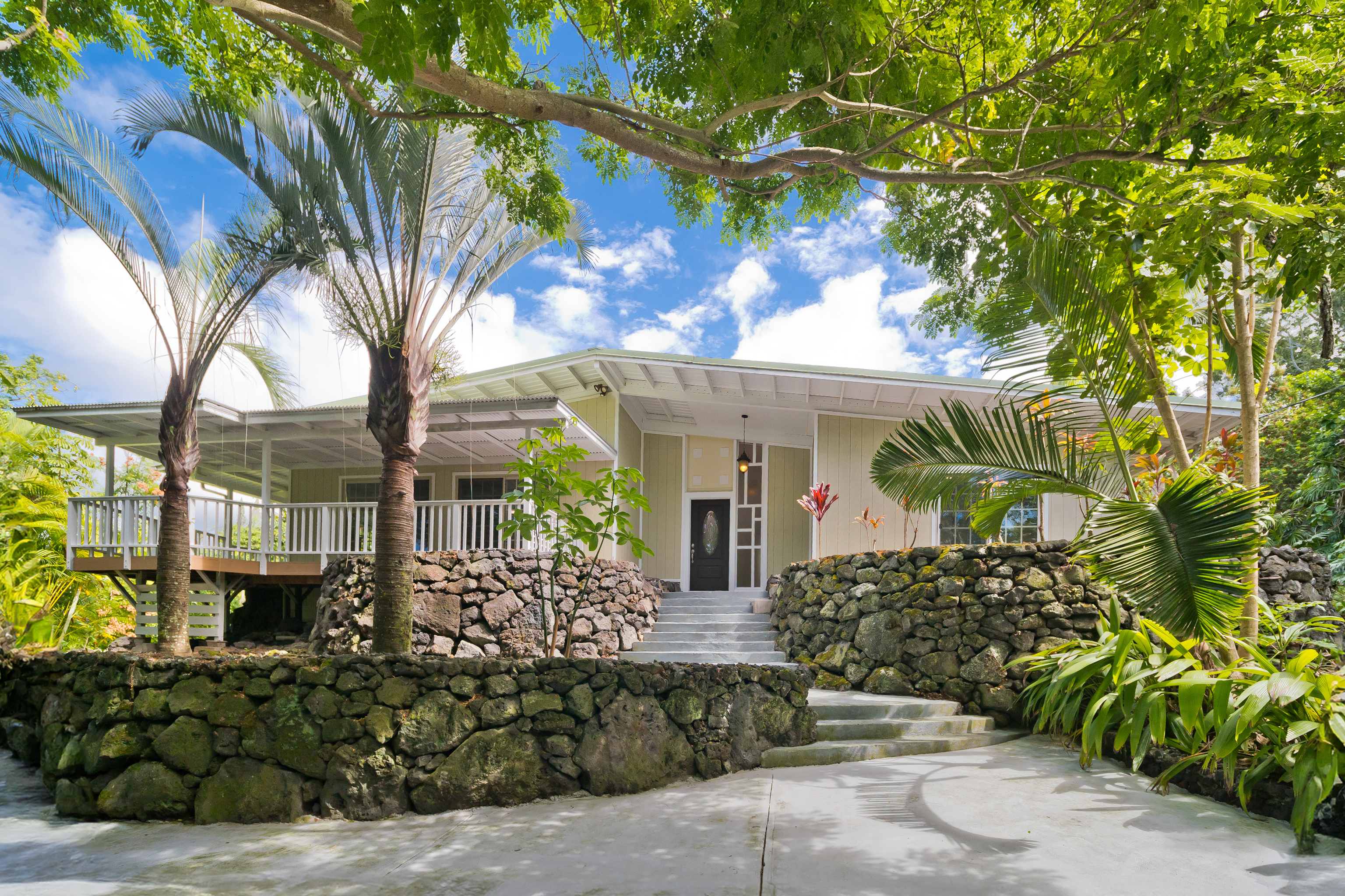 The western side of this impressive home with tasteful rockwalls and majestic palms and monkey pod trees.