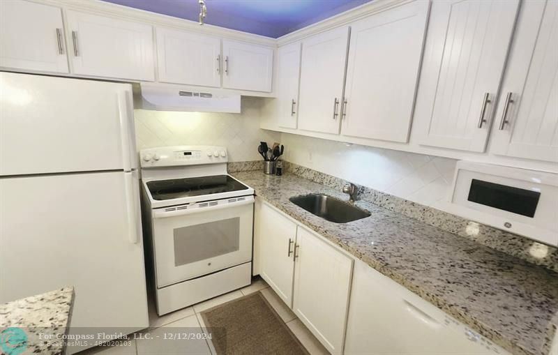 a kitchen with granite countertop white cabinets and white appliances