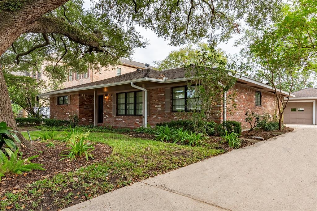 a view of a house with brick walls plants and large tree