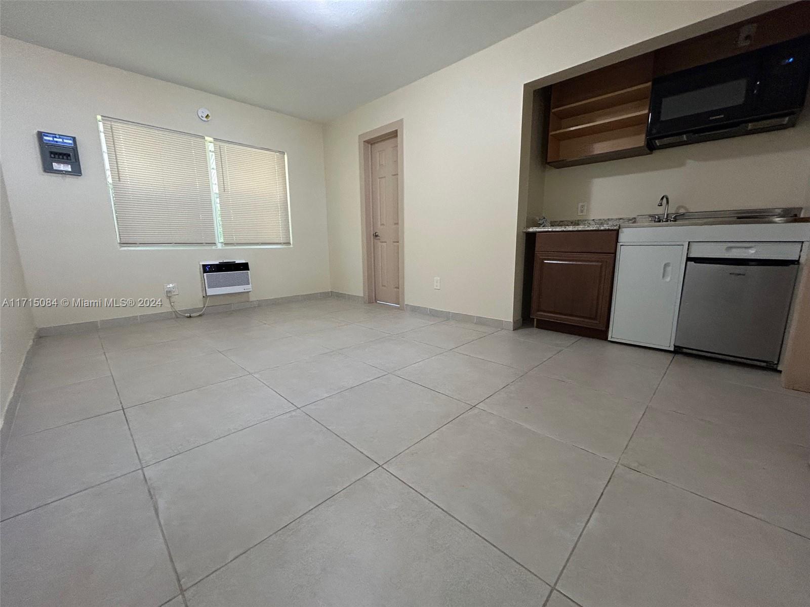 a view of an empty room with kitchen and window