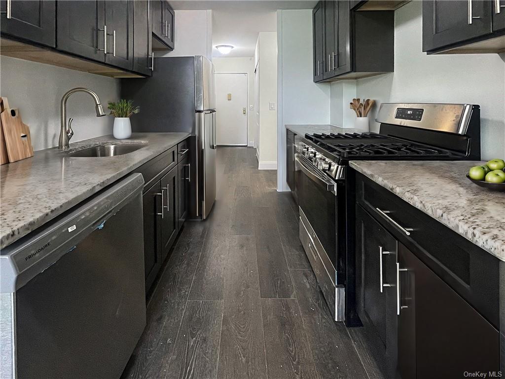 Kitchen with dark hardwood / wood-style flooring, sink, dishwashing machine, and stainless steel range with gas cooktop