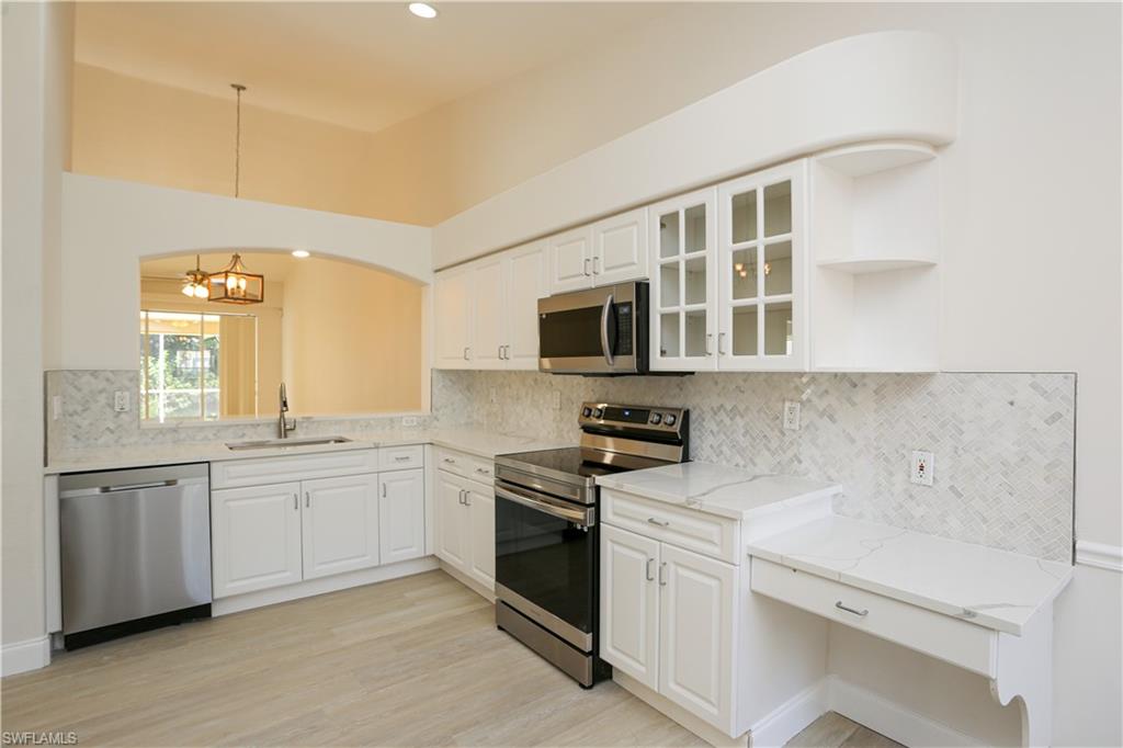 Kitchen with white cabinets, hanging light fixtures, appliances with stainless steel finishes, light stone countertops, and sink