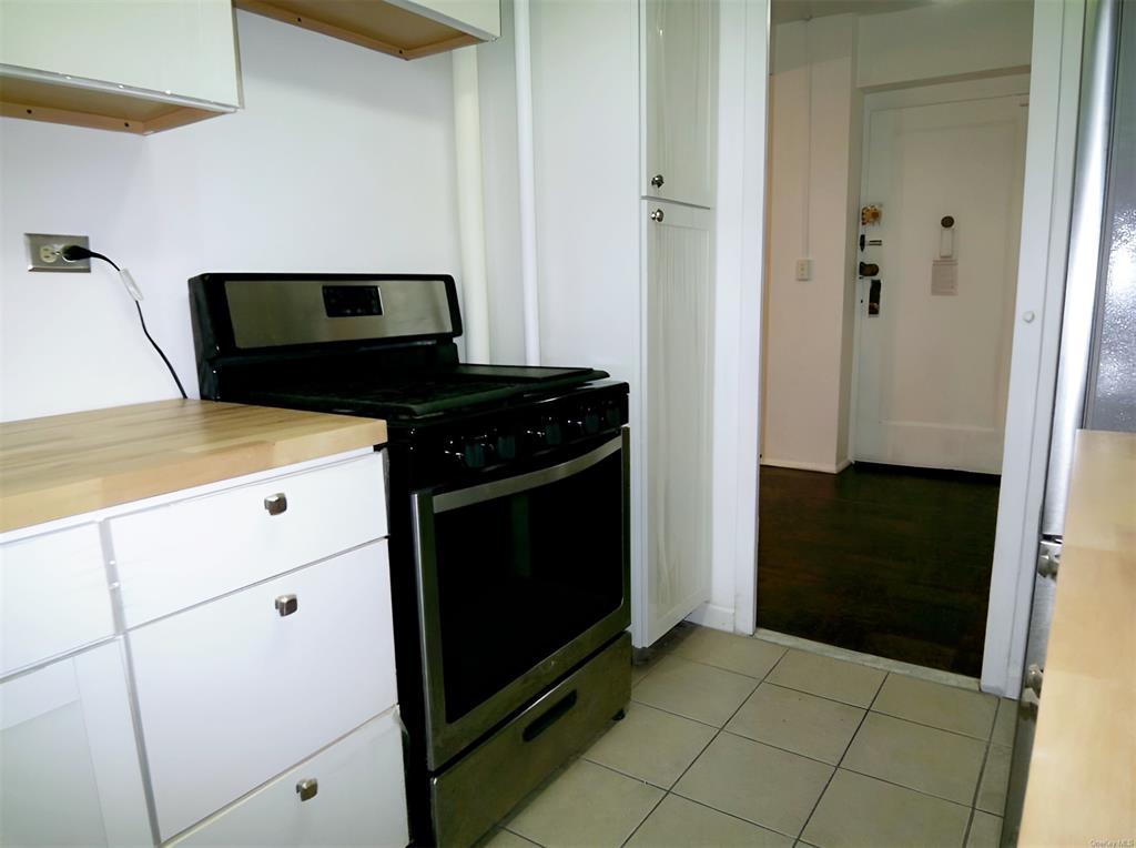 Kitchen with black gas stove, white cabinetry, and light tile patterned floors