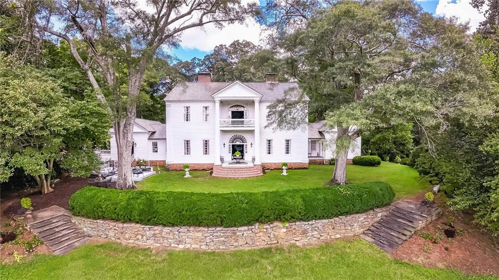 a view of a white house with a big yard plants and large trees