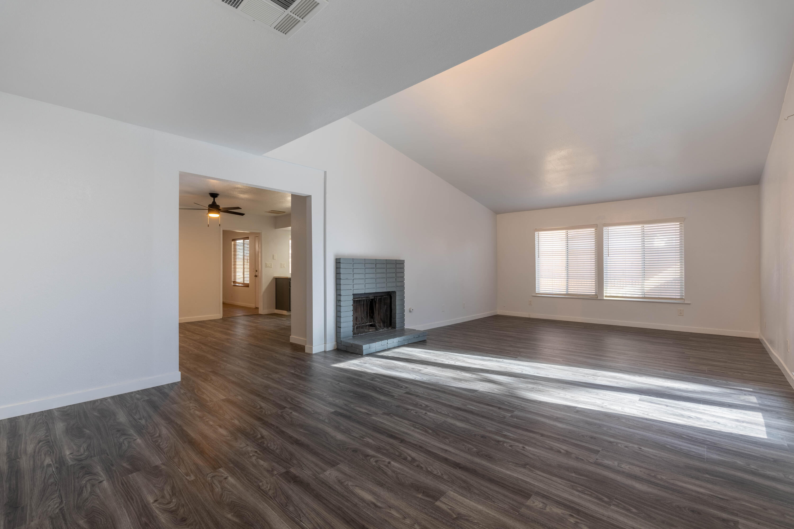 an empty room with wooden floor fireplace and windows