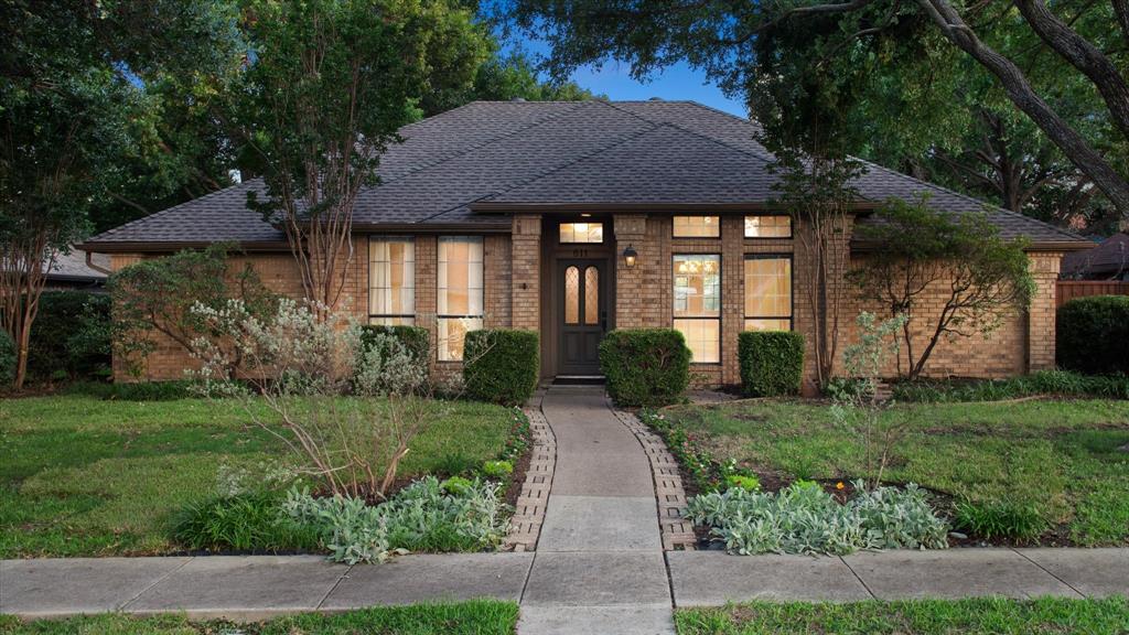 a view of a brick house with a yard plants and large tree