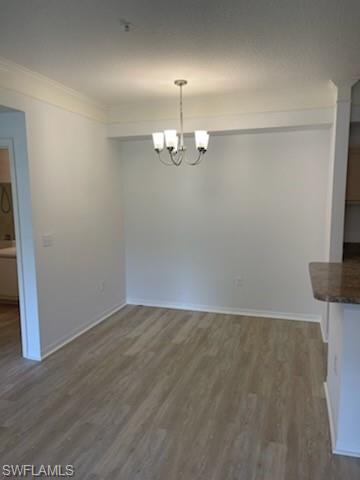 Unfurnished dining area with ornamental molding, dark wood-type flooring, and a notable chandelier