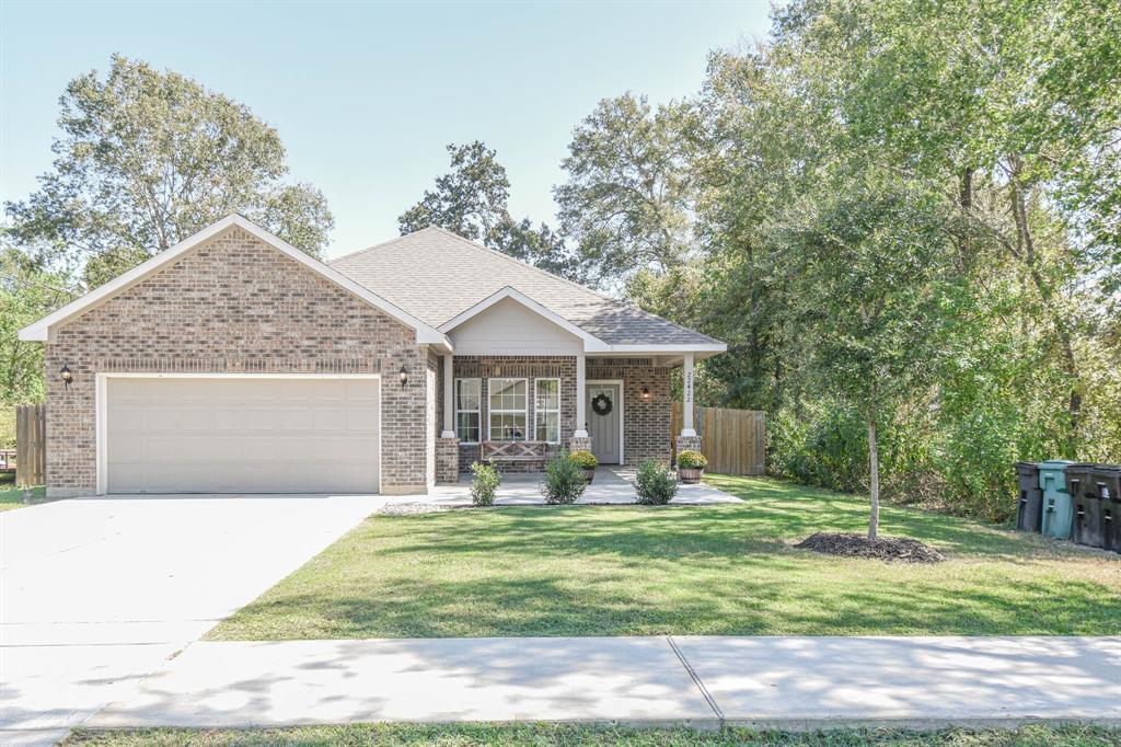 Charming single-story brick home with an attached two-car garage, neat landscaping, and mature trees offering privacy. The front entrance features a welcoming covered porch.