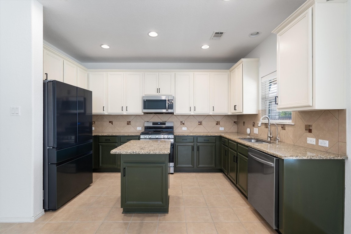 a kitchen with kitchen island granite countertop white cabinets refrigerator and stainless steel appliances